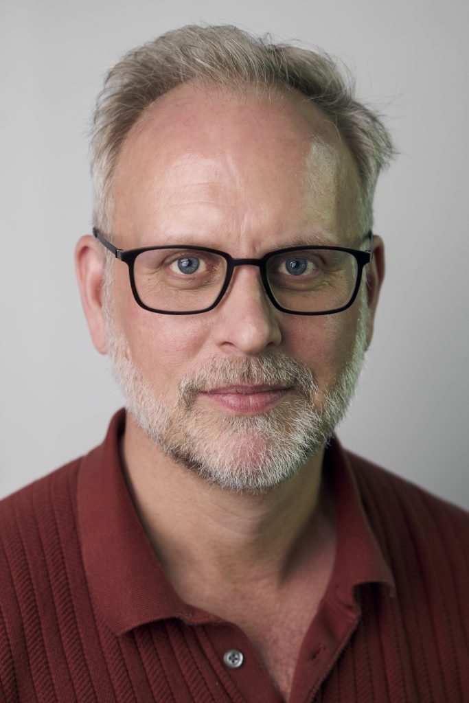 Steven Sparling, Founder of the Thriving Creative wears a burgundy shirt, black glasses and has a grey and white beard and hair. 